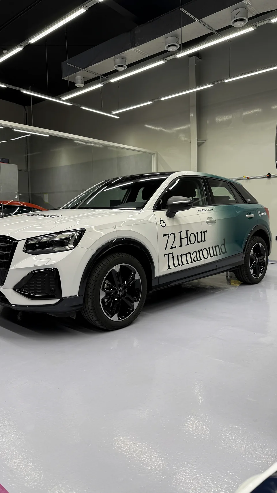 Front three-quarter view of a white Audi SUV with teal Genetiq fleet graphics